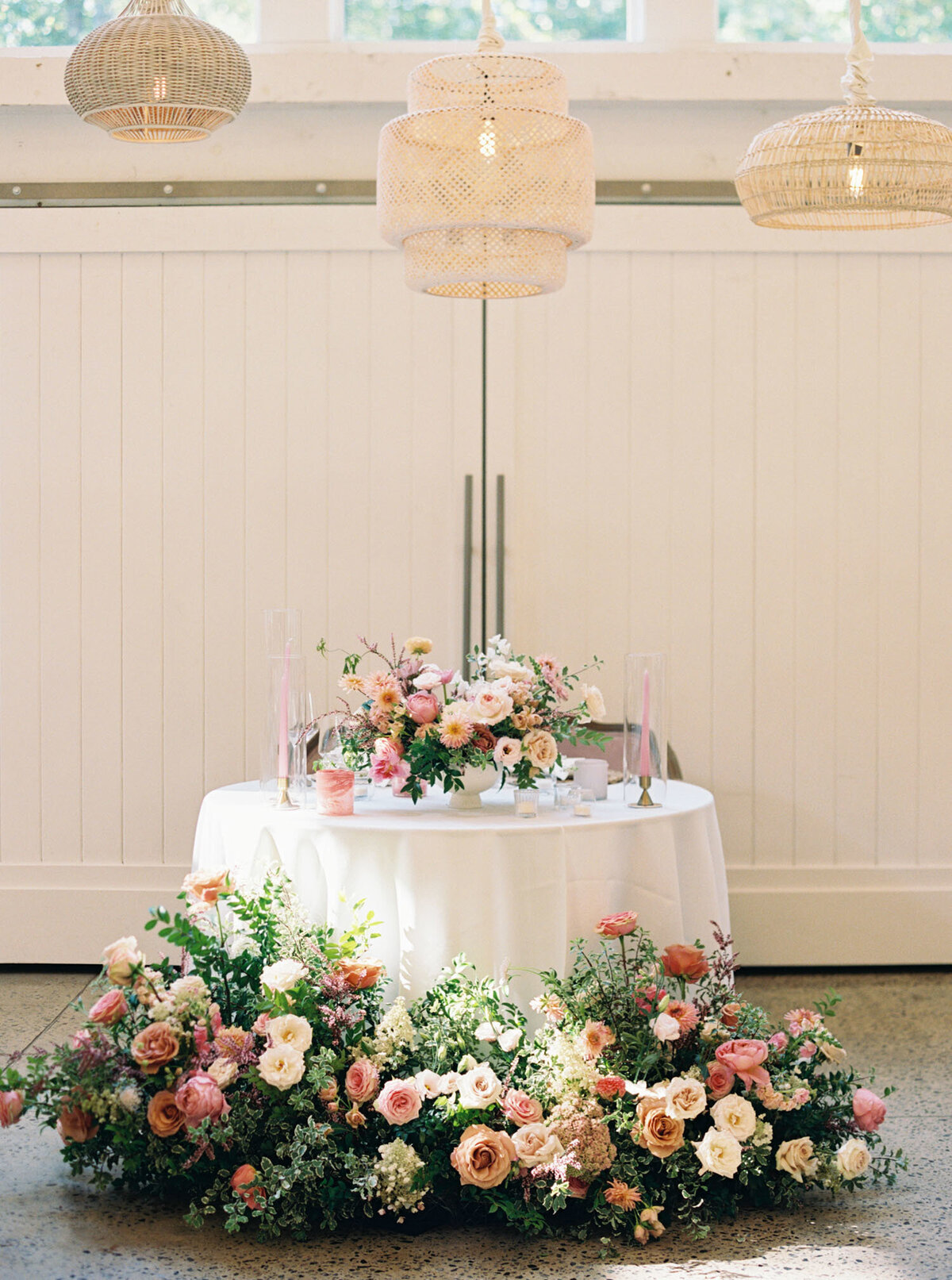 Lush floral centerpieces in hues of pink, peach, and cream. Styled candlesticks with pink tapers and colored glass candle holders. Sweetheart table with floral meadows surrounding the base of the table. Bright and colorful wedding design for fall weddings in North Carolina. Traveling floral designer for wedding in North Carolina. Design by Rosemary & Finch Floral Design in Nashville, TN.