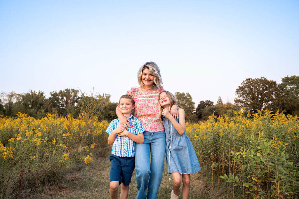 Mom holds kids tightly while smiling and walking toward camera in Canton Michigan flower field