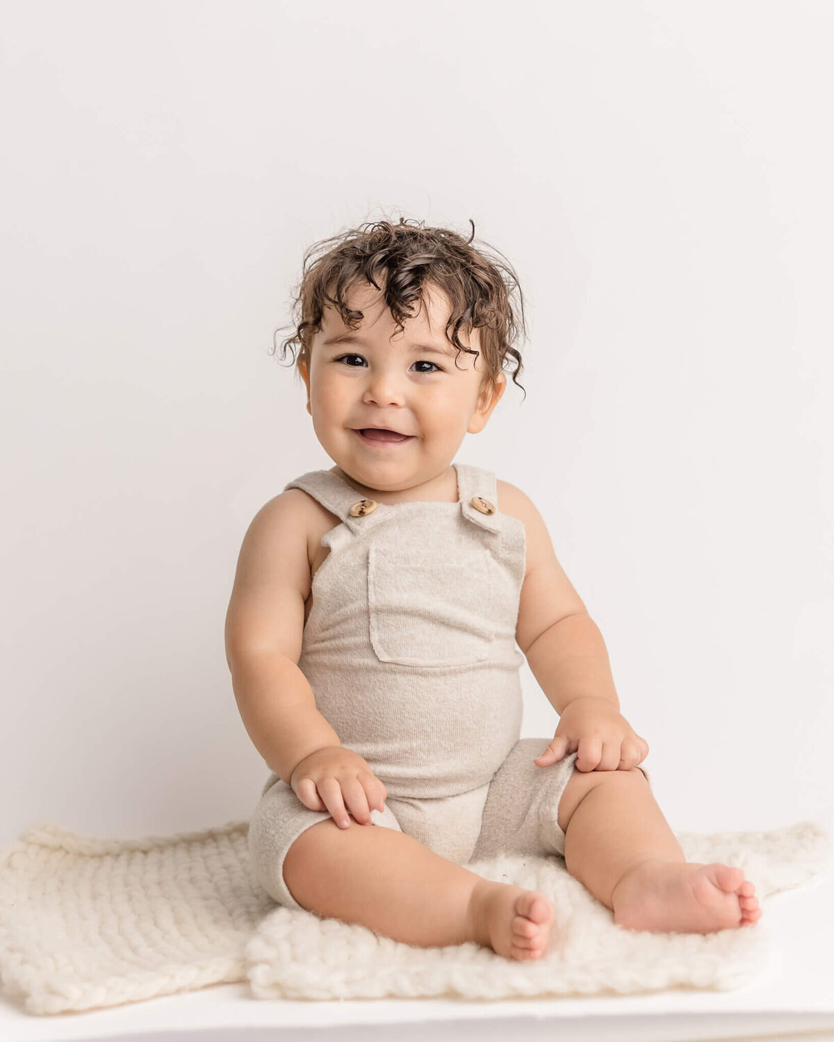 baby boy with brown curly hair giving the biggest smiles in all white photo session for his first birthday. Taken by portland milestone photographer Ann Marshall