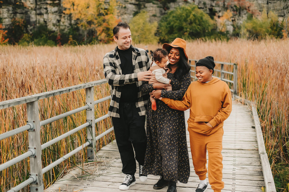 Family smiling on a bridge at their fall mini Family Photographer session near Hamilton, ON.
