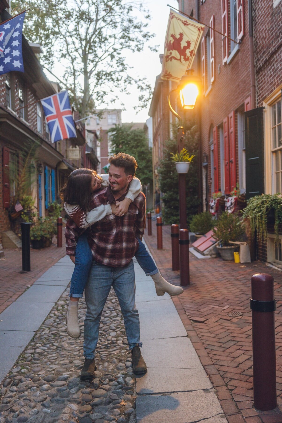 Playful piggyback ride on cobblestone street lined with old brick houses.