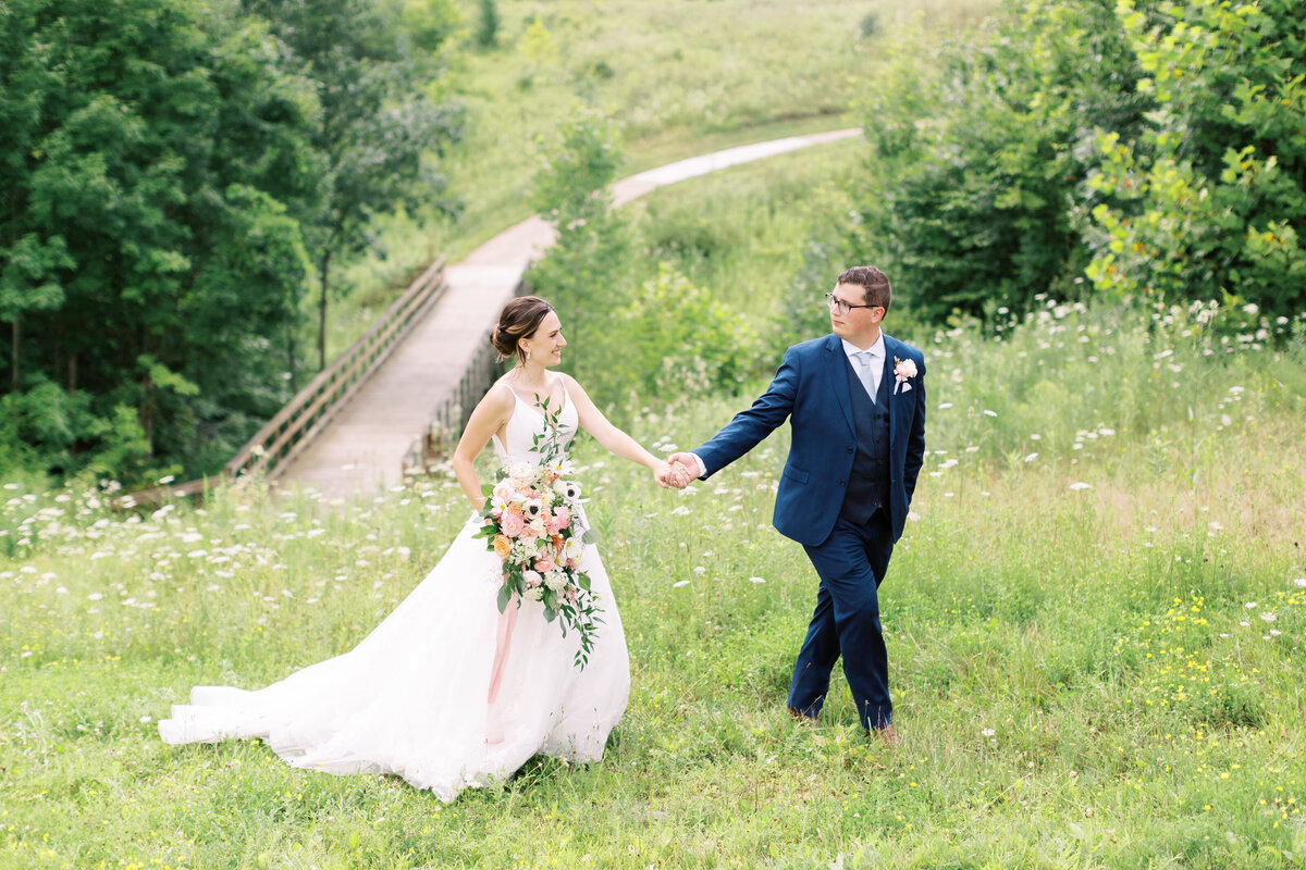 bride and groom walking holding hands in field