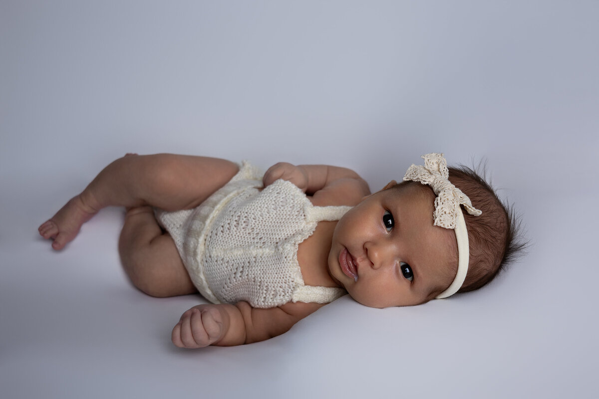 Newborn laying on a white backdrop. She is looking at the camera with her ankles crossed.