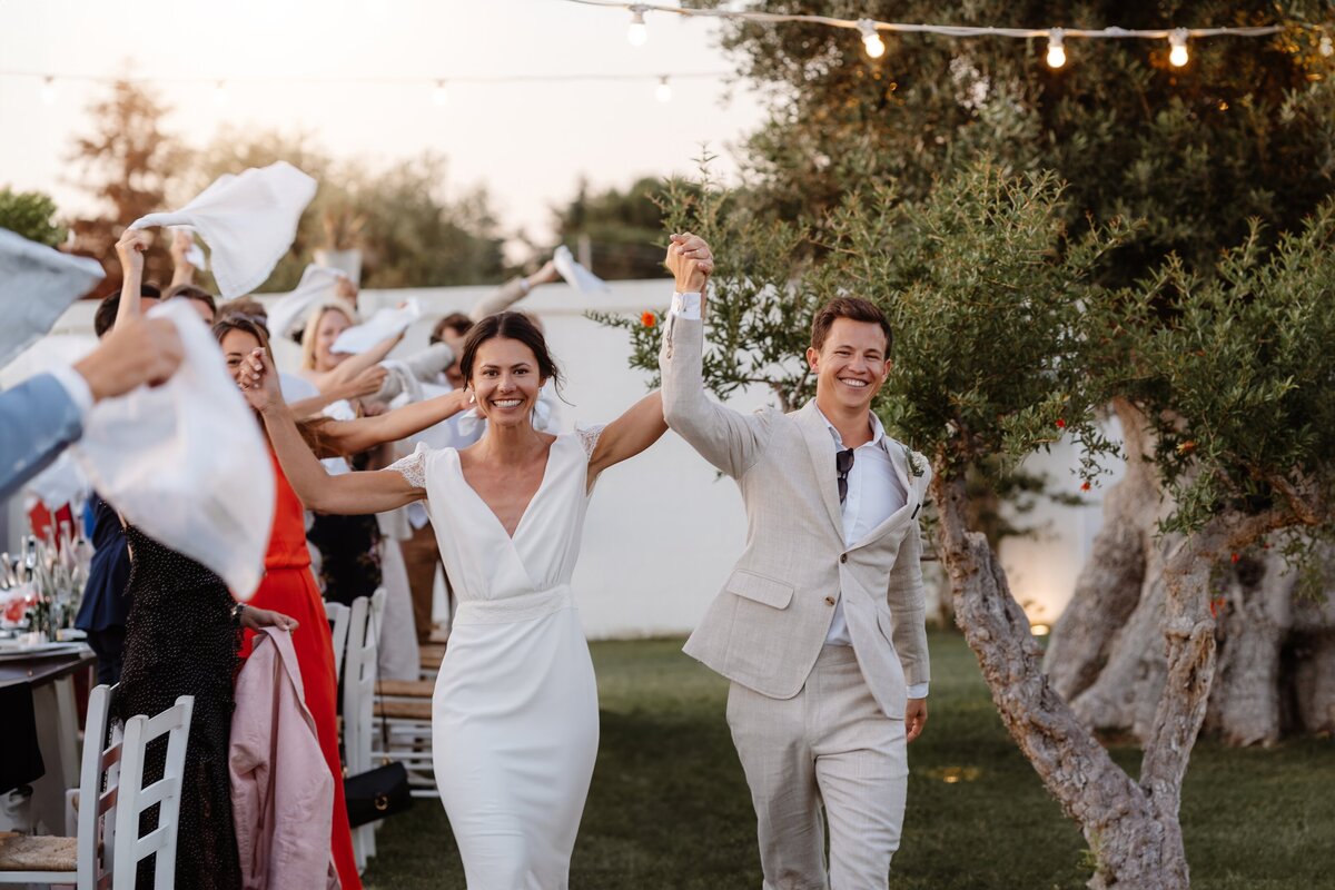 Bride and Groom making their entrance to their alfresco wedding breakfast in Italy, guests twirling their napkins in the air