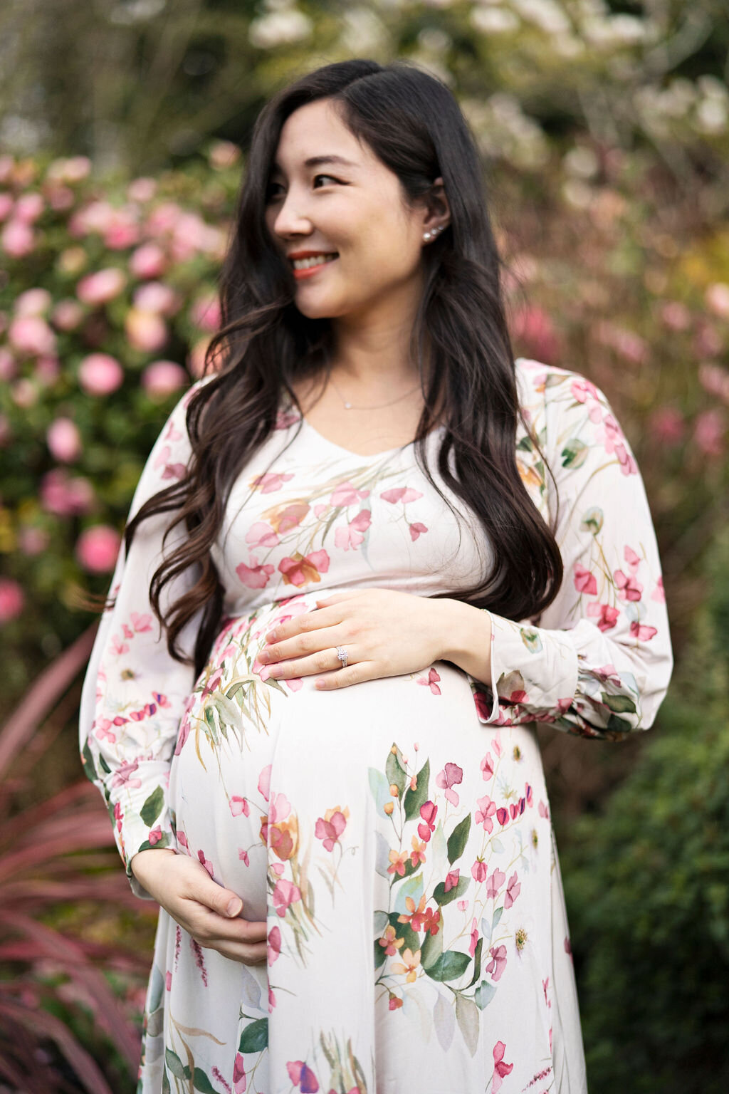 Pregnant lady wearing flowery dress standing against a backdrop of spring flowers during a springtime photoshoot