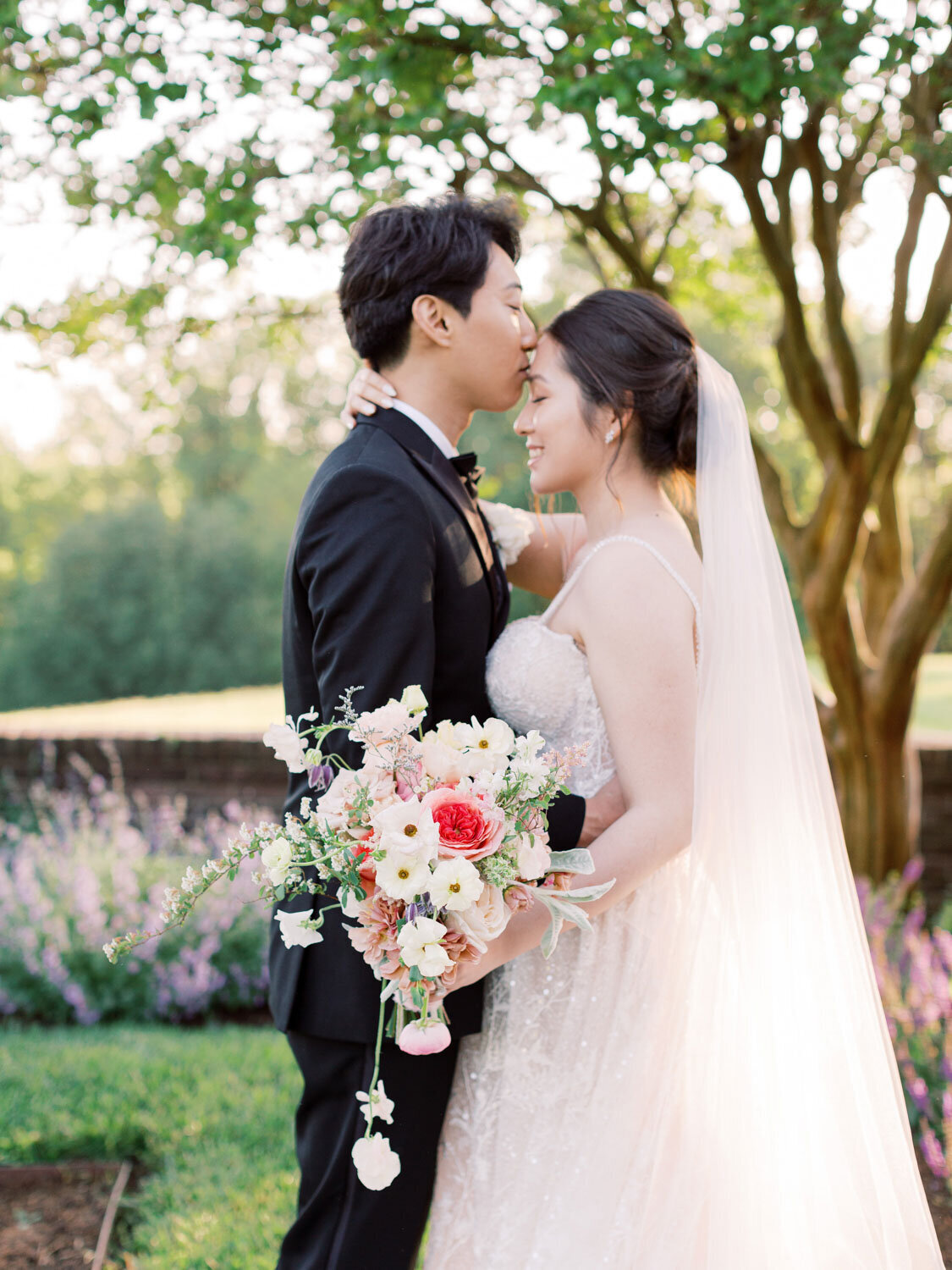 Groom kissing bride’s forehead in the garden