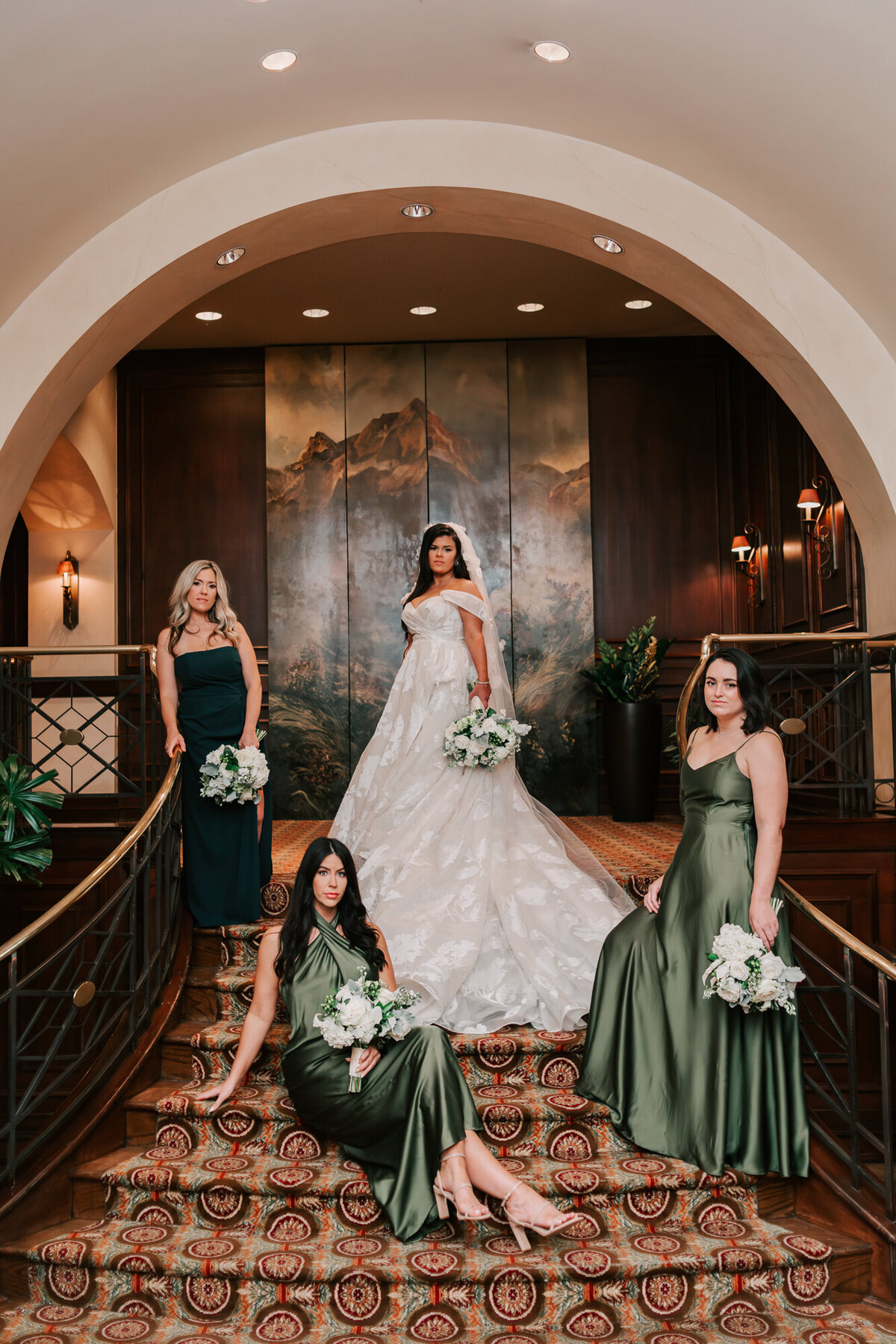bride and her bridal party stand and sit on the staircase for portraits before their ceremony