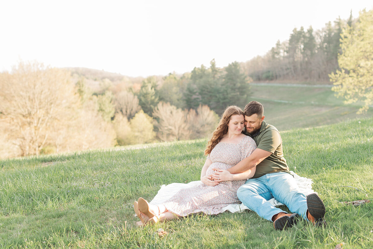 Pregnant couple snuggled up together on a blanket in the Blue Ridge Mountains during maternity portraits
