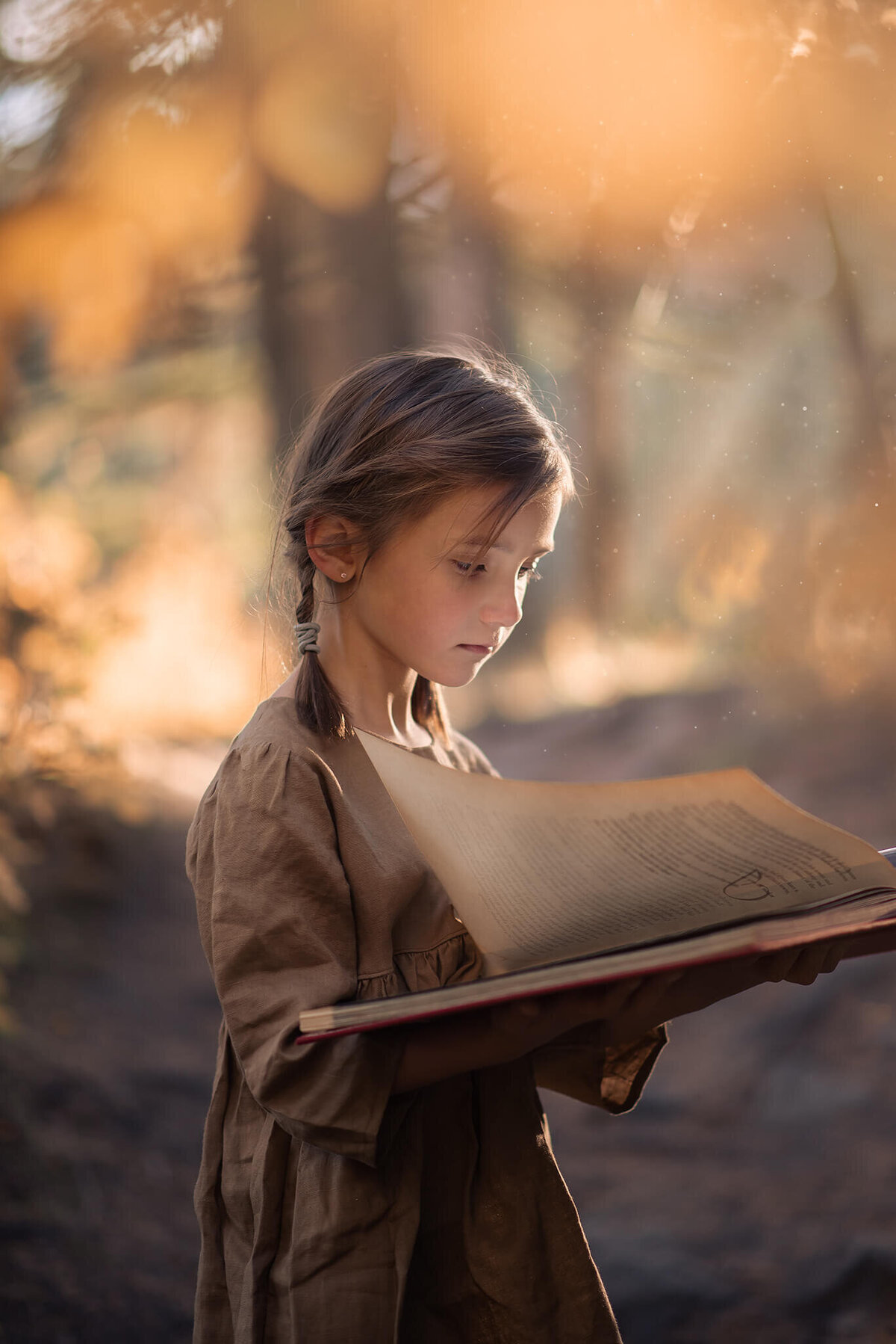 Little girl stands holding a large book open with sun rays beaming down in Kamloops, BC.