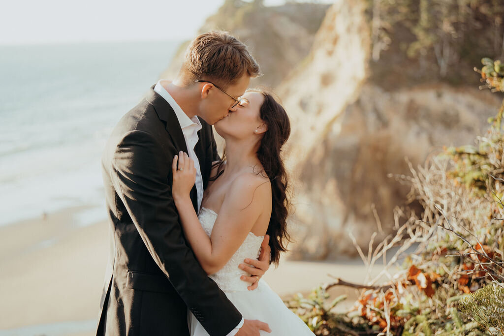 a bride and groom kissing on the beach in the sunlight