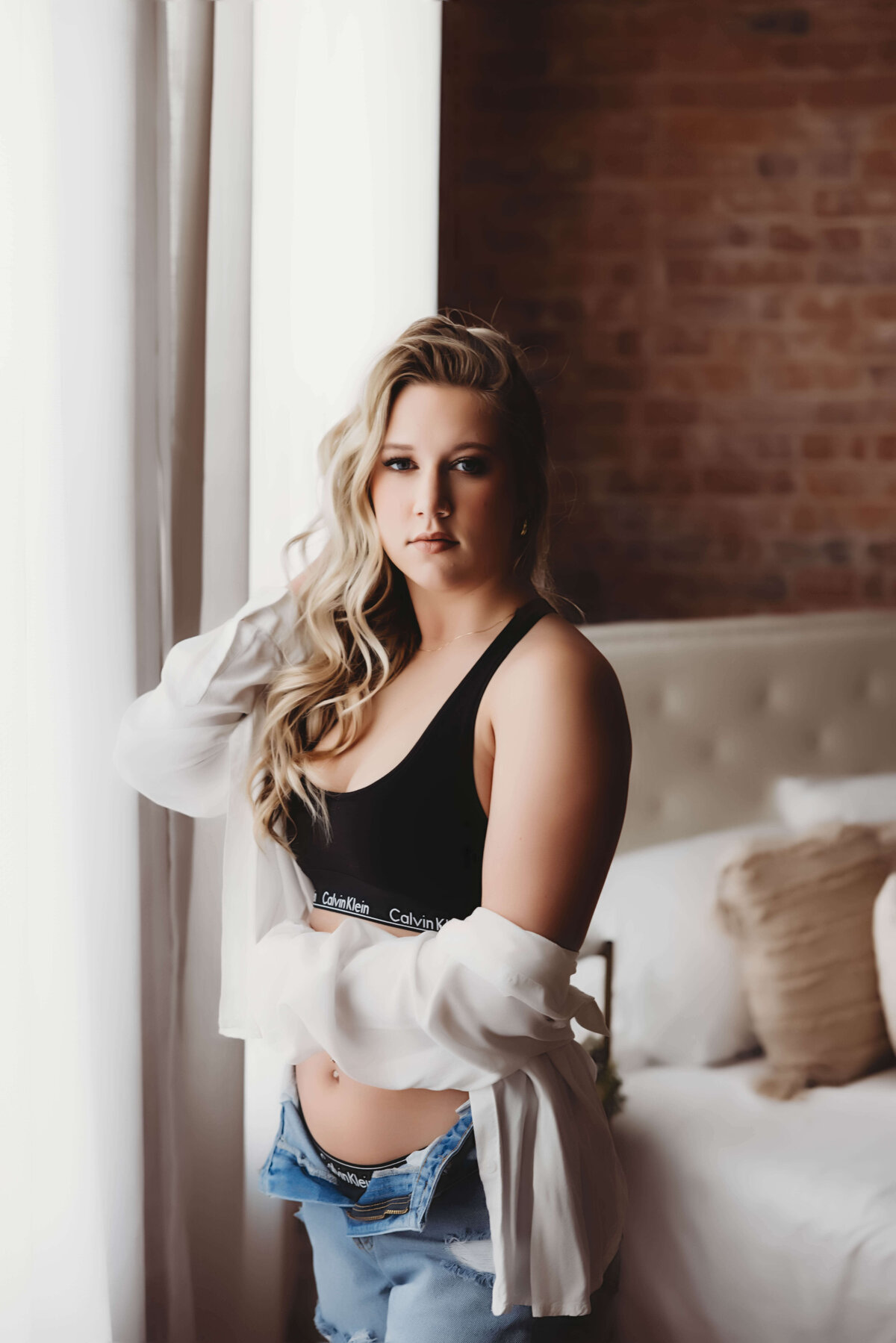 Woman standing by window in Calvin Klein and jeans for boudoir session with Reva Davis photography