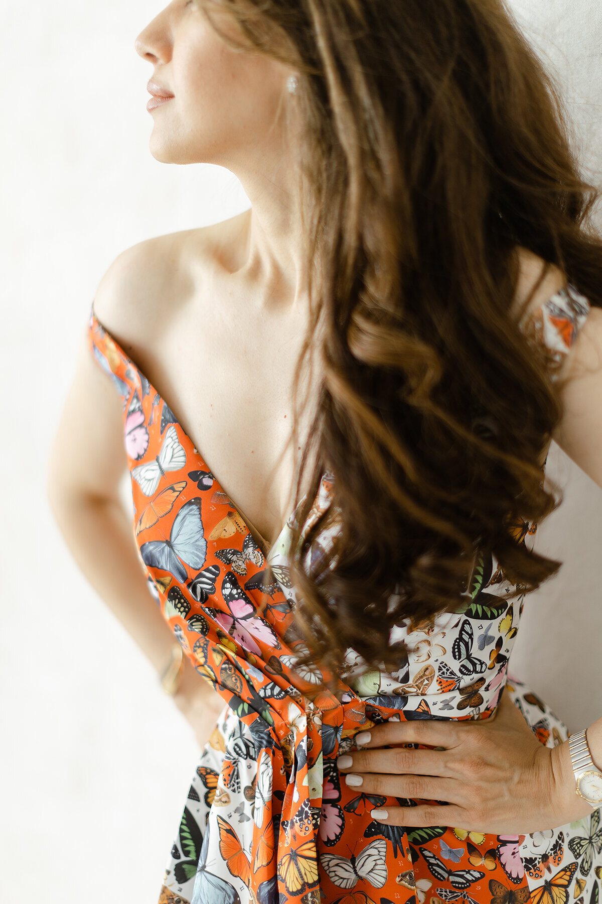 A cropped in photo of a woman posing fiercely for her boudoir photos as she wears a colorful butterfly dress with her hands on her hips and looks out of the Dallas photography studio.