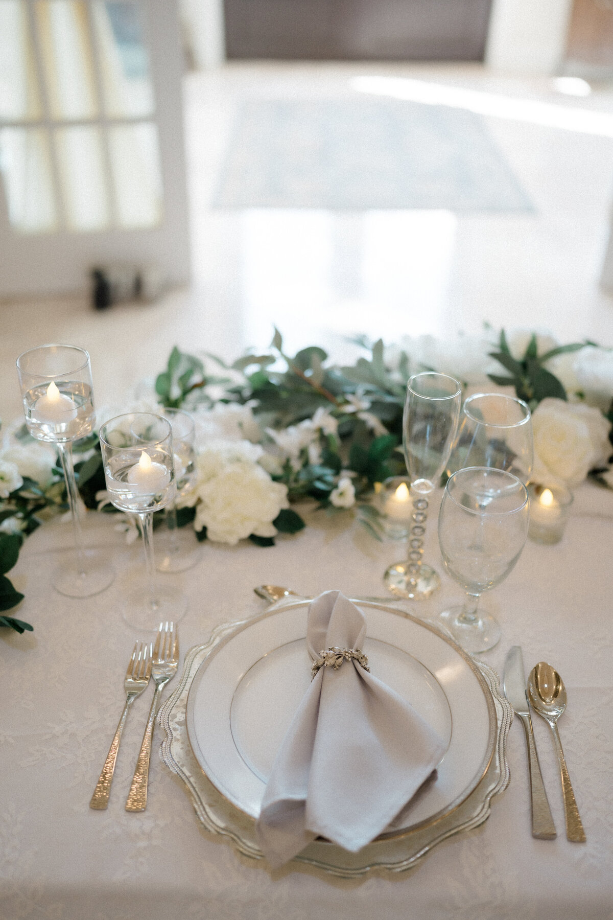 Elegant sweetheart table featuring white and silver silverware, fine china, and a floral arrangement of white roses and peonies, designed by In Full Bloom Event Planning & Design