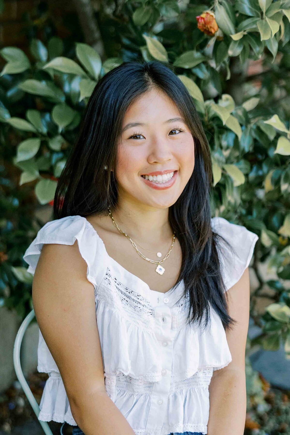 Asian girl wearing a white top and sitting at a vintage table with greenery in the background