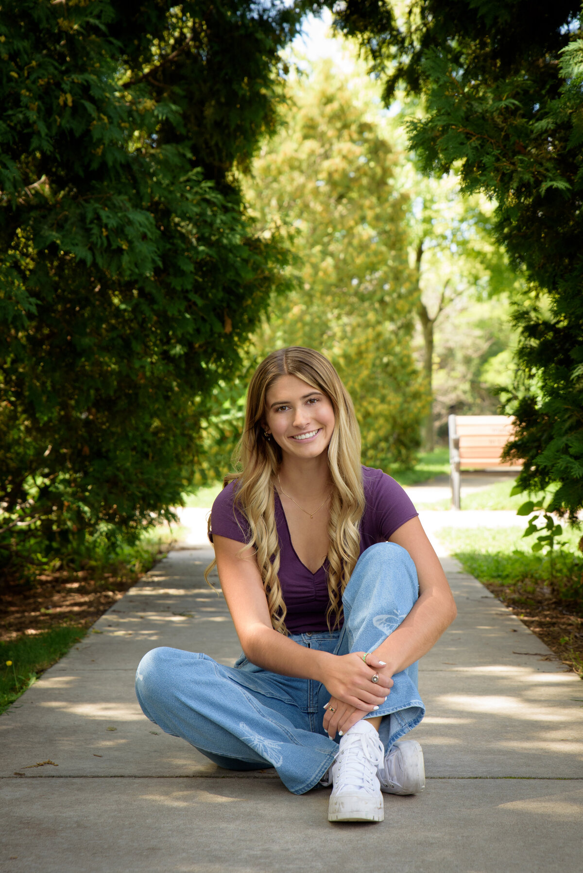 De Pere High School senior girl wearing a purple shirt and jeans sitting on a sidewalk in Voyager Park in downtown De Pere, Wisconsin