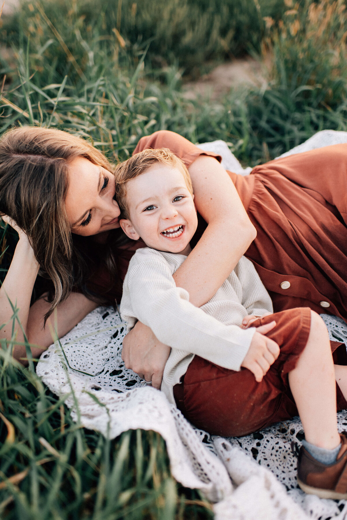 mom lying in the grass snuggling her son while he giggles