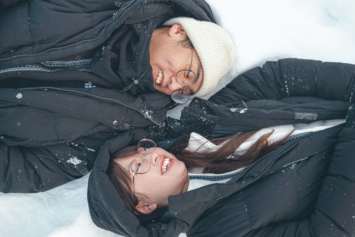 Couple lying together in thick Banff snow sharing laughs and love.