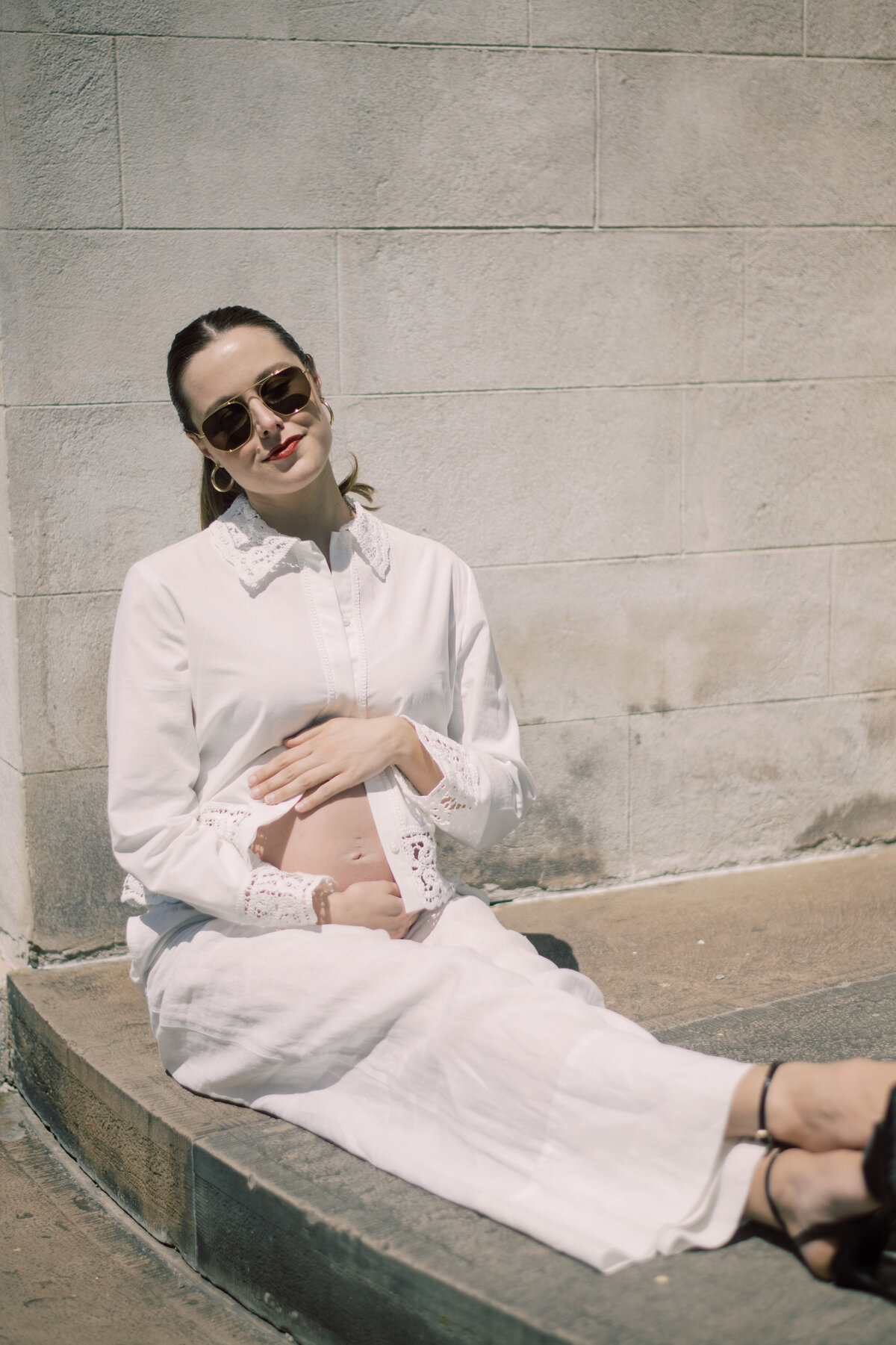 Full-length maternity portrait of a poised mother-to-be in white Zara attire, standing beneath golden columns