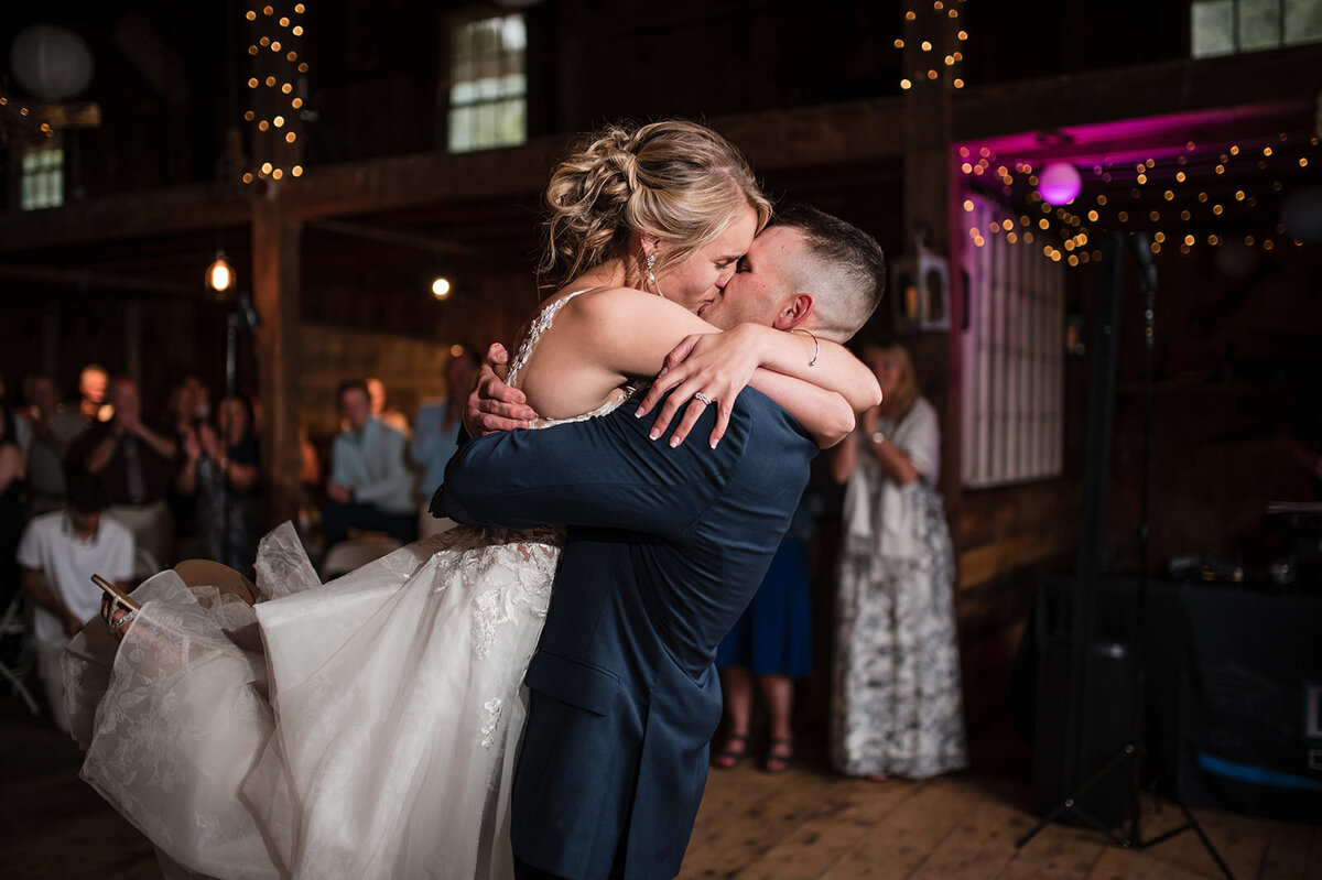 A groom hugging a bride and lifting her up as they kiss.