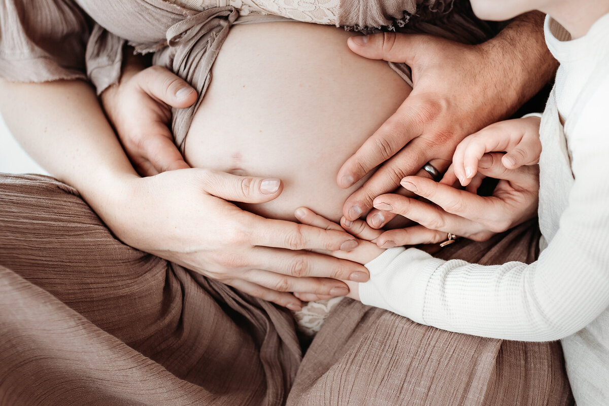 close up picture of pregnant belly with mom dad and brother's hands on bare belly