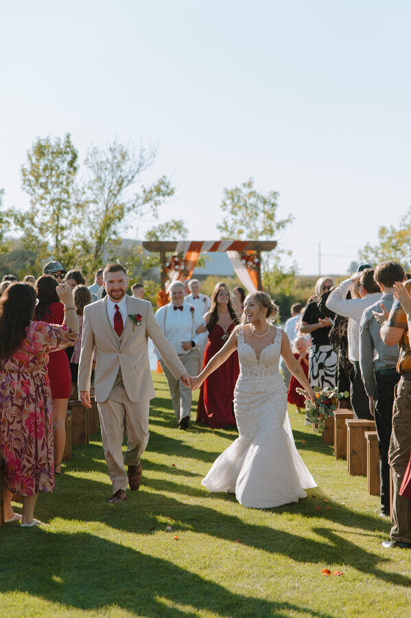 A bride and groom walk down the aisle after just getting married. Their ceremony is outside in a grass field in eastern Idaho.