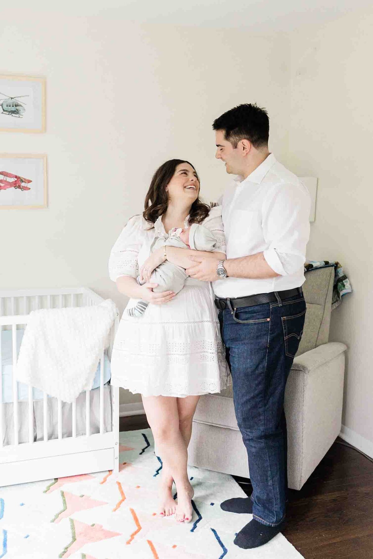 New parents snugging in front of crib with newborn