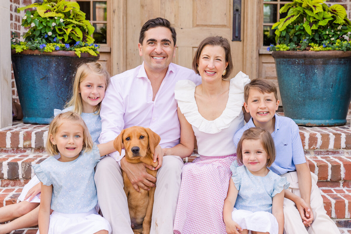 family with four young  children and a dog sitting on their house front steps wearing light blue and white outfits  | Atlanta GA family Photographer | Laure Photography