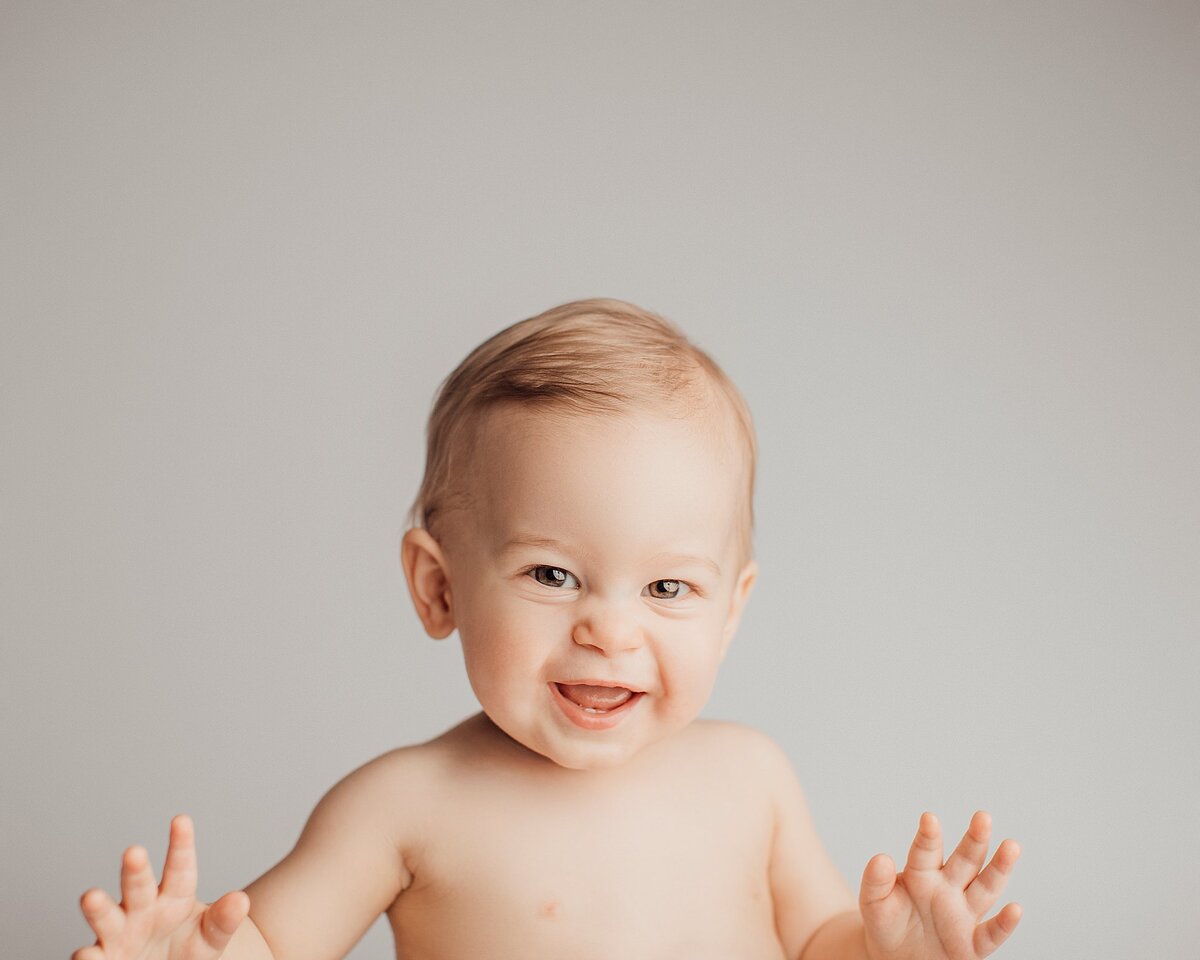  Baby reaching toward camera with big smile during interactive photo session