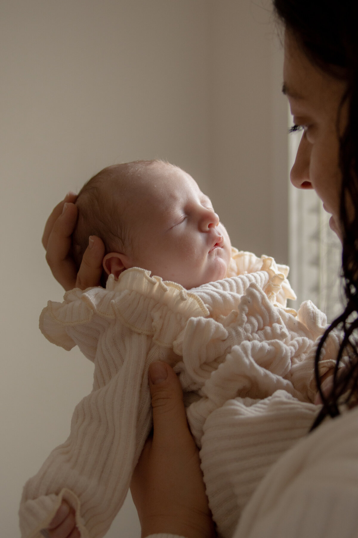 mother lovingly looking at newborn daughter while she sleeps in her hands