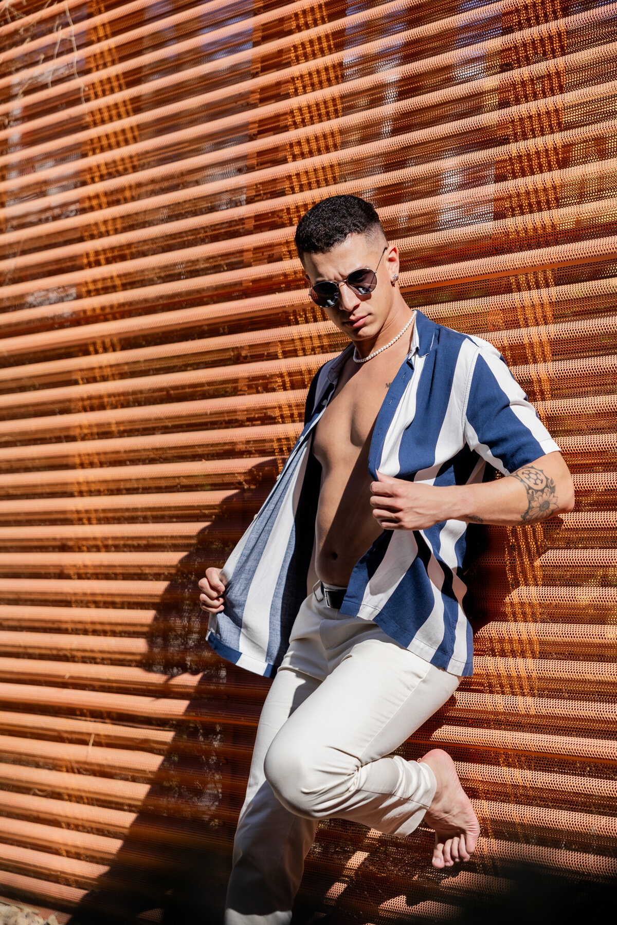Editorial portrait of male model in striped shirt and white pants against wood-paneled architecture in Palm Springs.