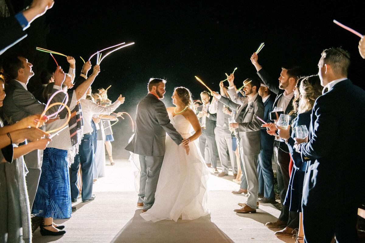 Bride and groom embrace during wedding exit surrounded by friends with glowsticks