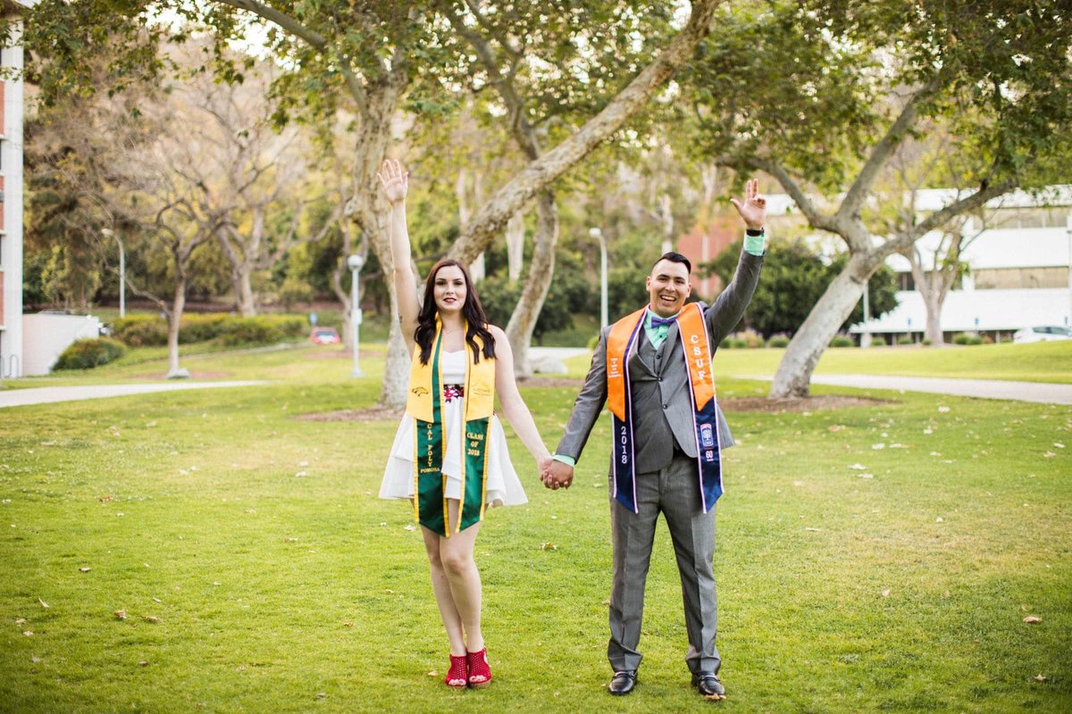College graduates hold hands and raise their hands in the air during their grad photos photoshoot