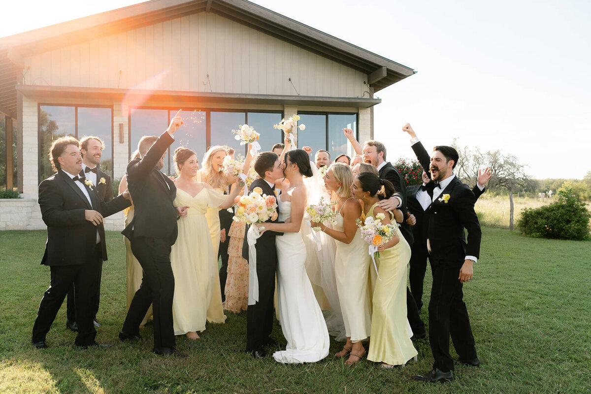 the bridal party crowds around the couple as they kiss