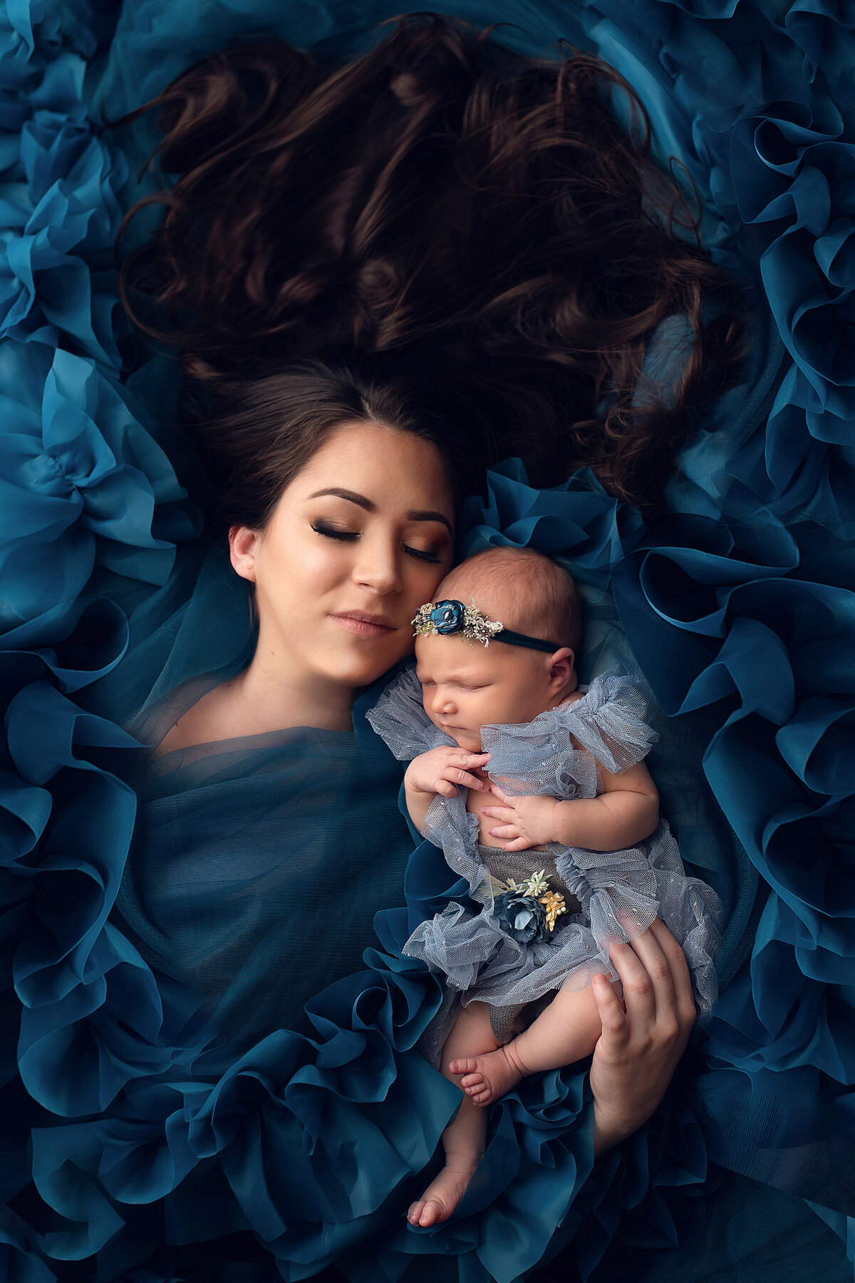 Portrait of mother and newborn daughter laying in a pile of teal ruffles.