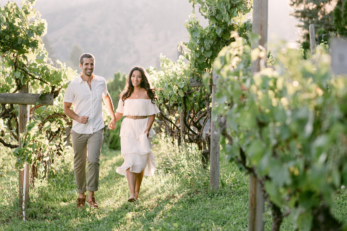 Engaged couple running through vineyard at Beecher Hill House