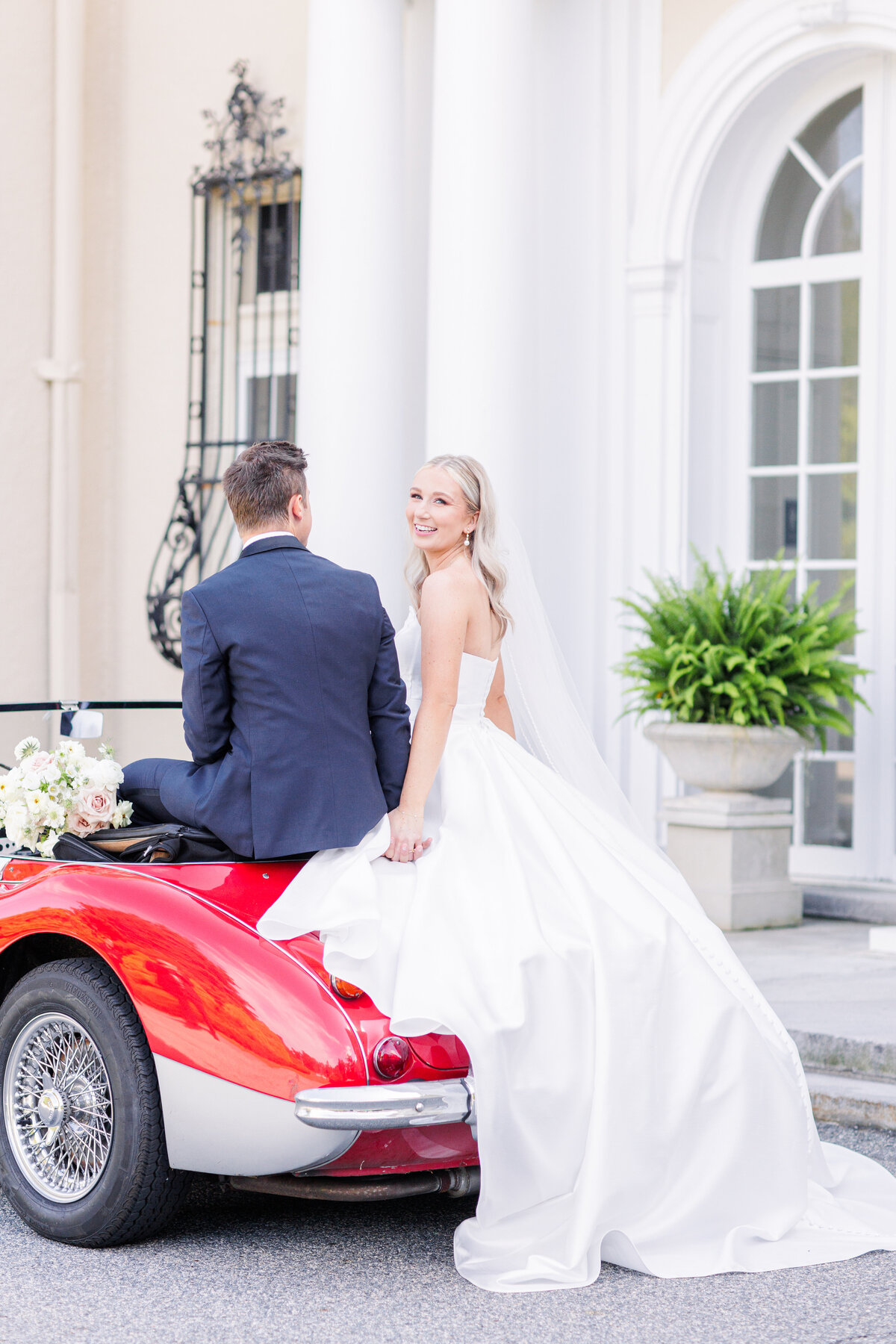 Bride and groom sitting on an antique car and holding hands representing editorial Boston wedding photography
