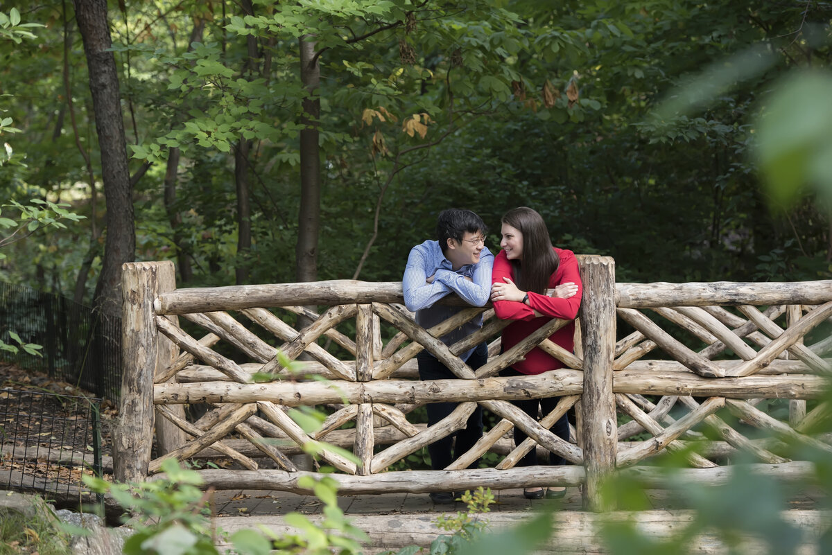 A couple standing next to each other as they lean over a wooden railing 