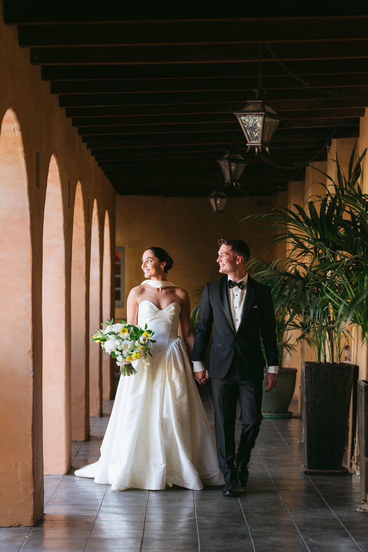 Bride and groom walking hand in hand through arched hallway at Royal Palms captured by Phoenix wedding photographer during a luxury Scottsdale wedding.