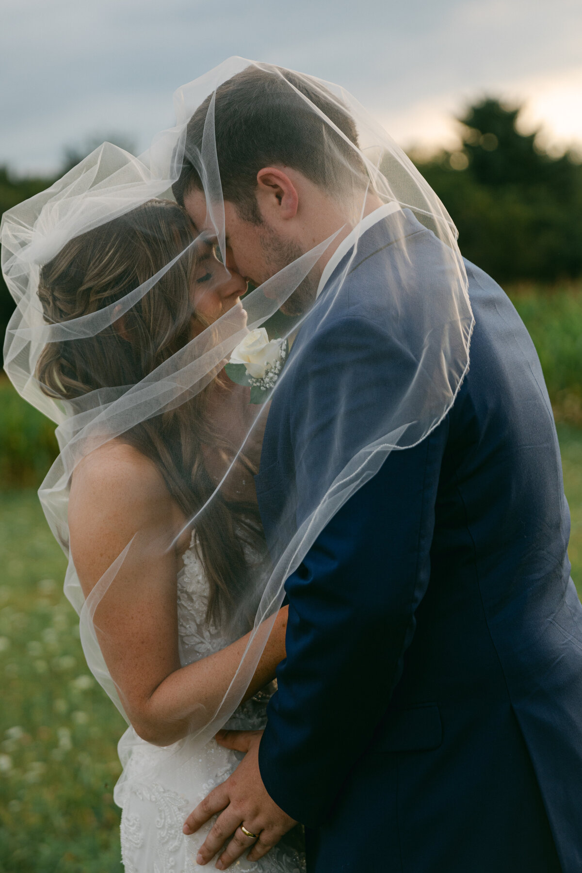 bride-groom-kiss-under-veil-field-sunset