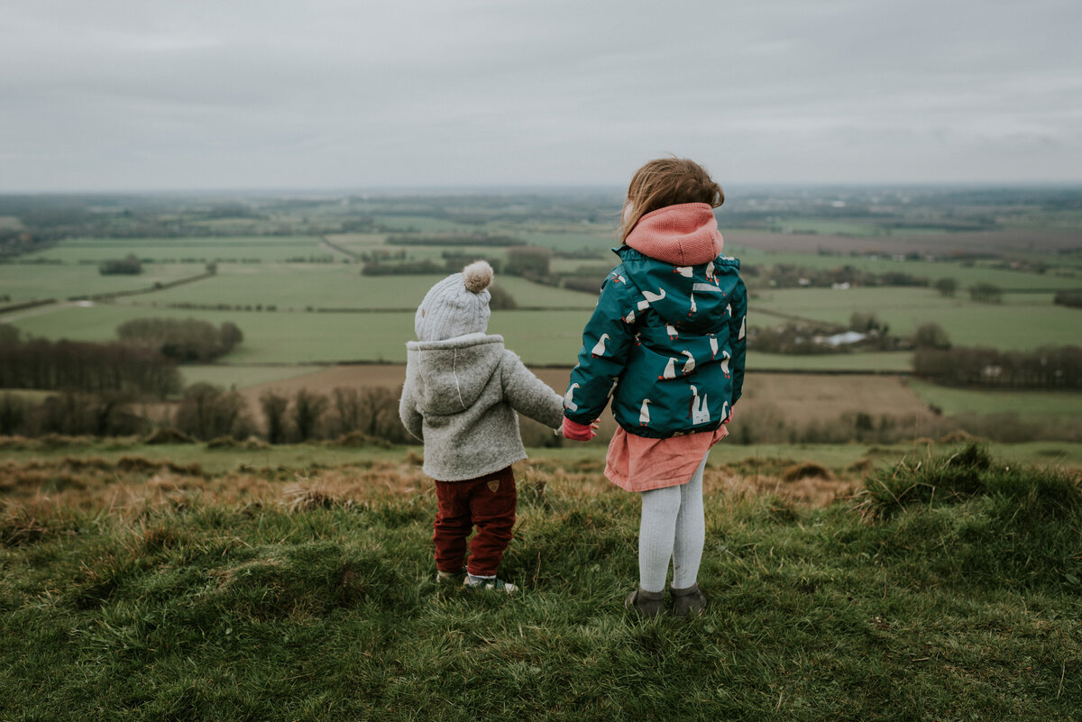 siblings in winter coats holding hands in the country