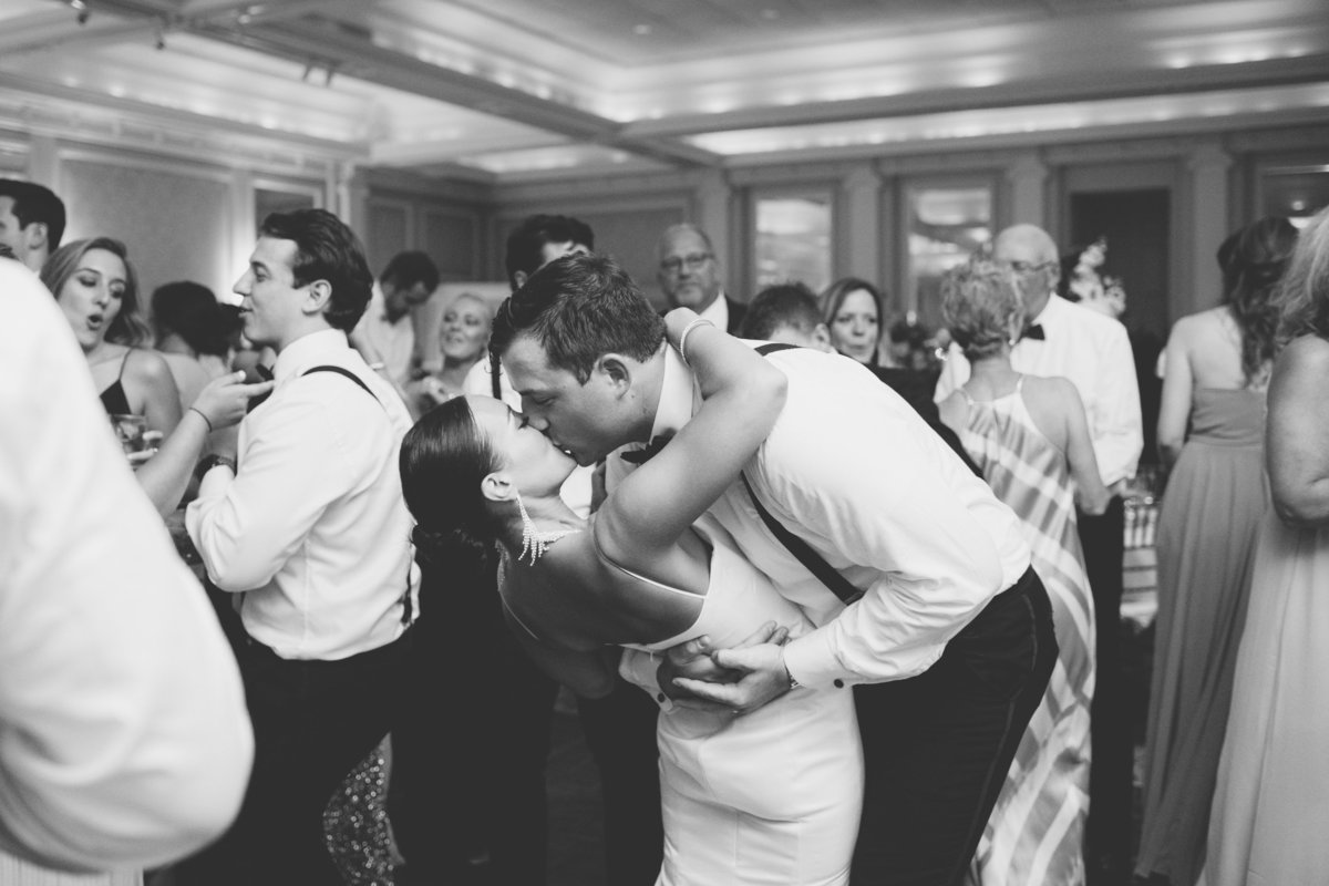 black and white photo of bride and groom kissing on the dance floor during wedding reception at The Muttontown Club