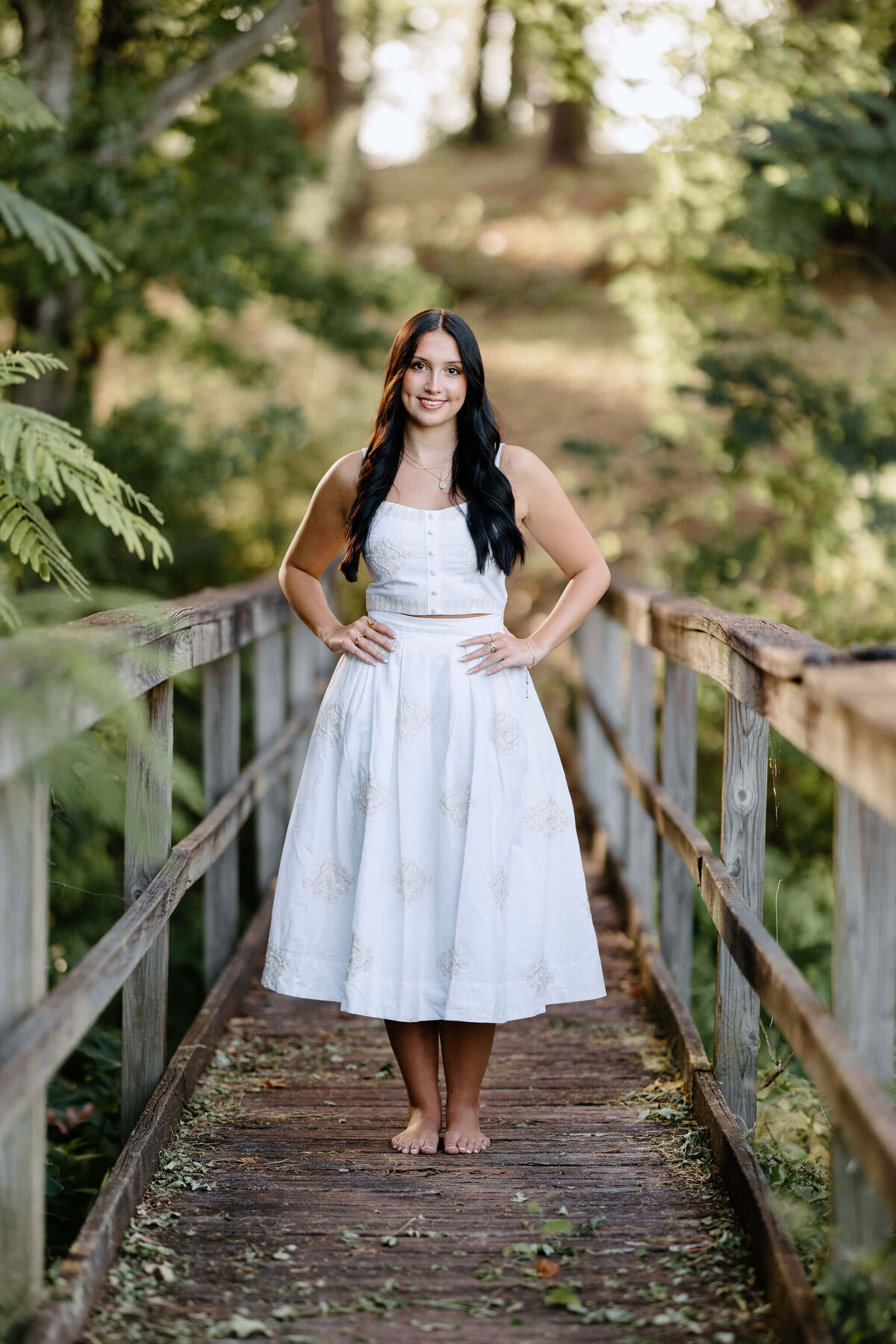 High school graduate wearing white long dress standing on bridge in East Texas area