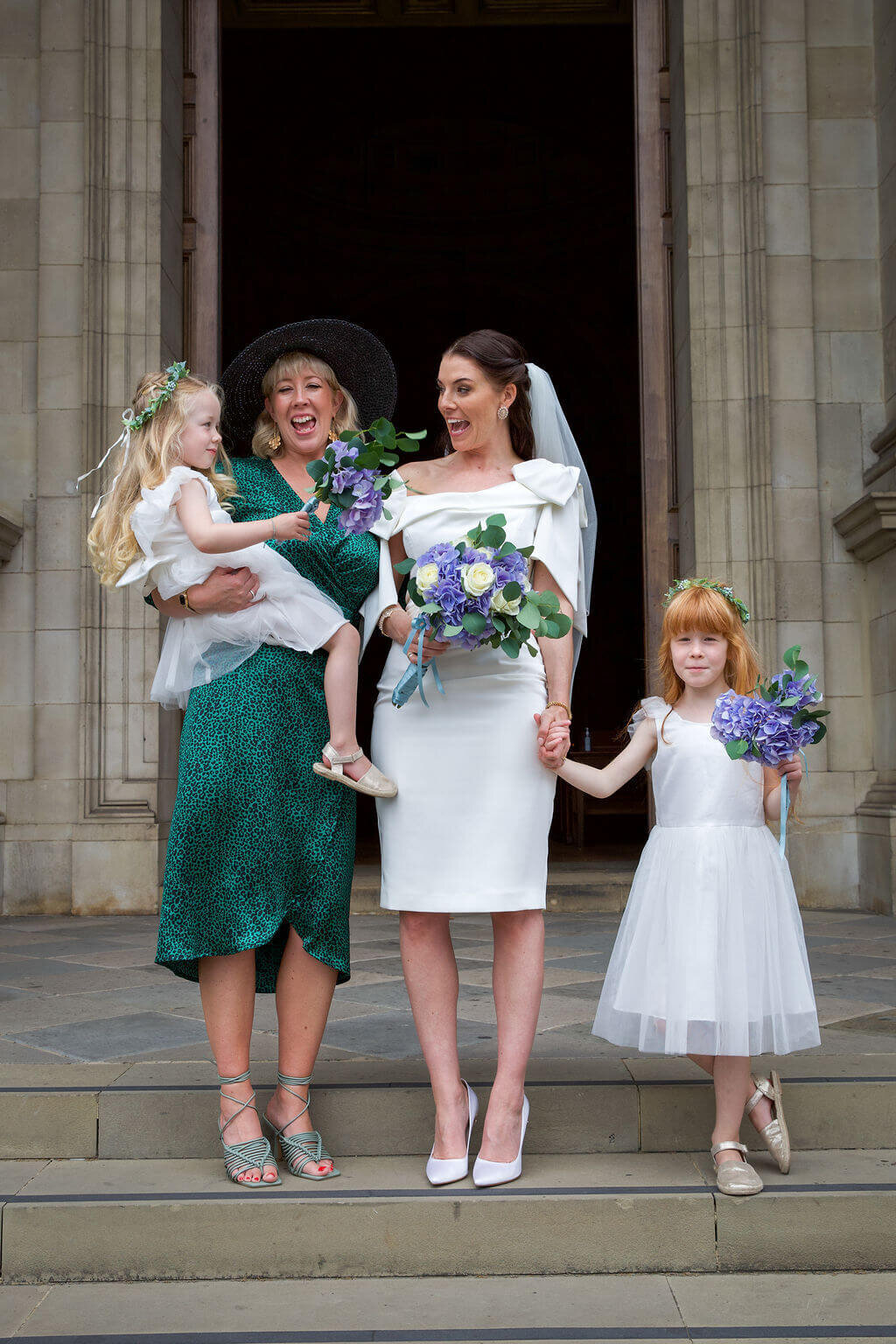 Bride laughs with flowergirl for posed group shot