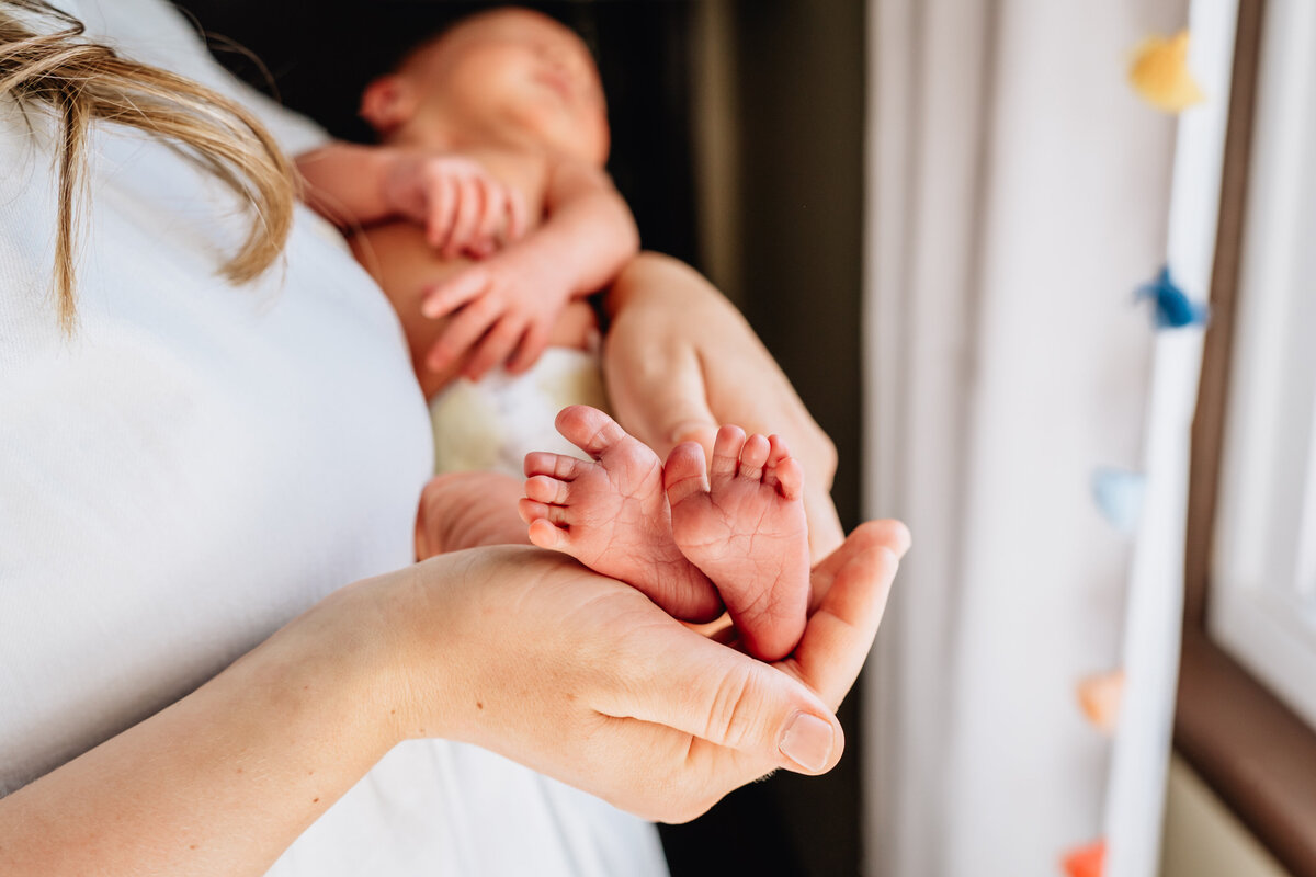 A close-up of a mother cradling a newborn, with the focus on the baby's tiny feet resting in the mother’s hand.