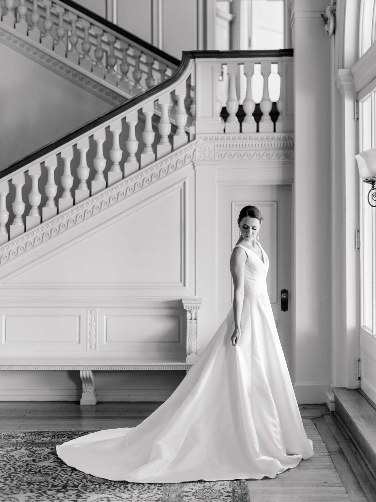 Bride in classic satin gown standing beneath the grand staircase at Cairnwood Estate, captured by Philadelphia fine art wedding photographer Elizabeth Kane.