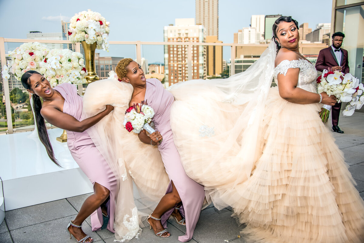 Bride on rooftop in atlanta and bridesmaids holding her dress 