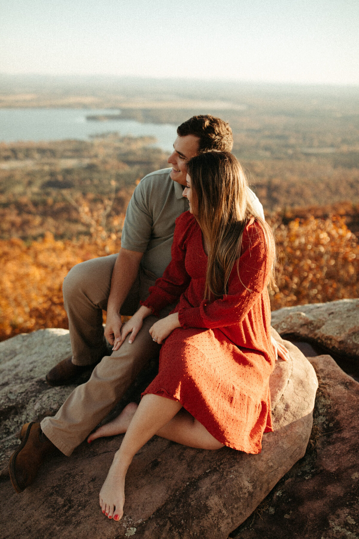 A couple is sitting on a rocky overlook together while they look out over the fall landscape.