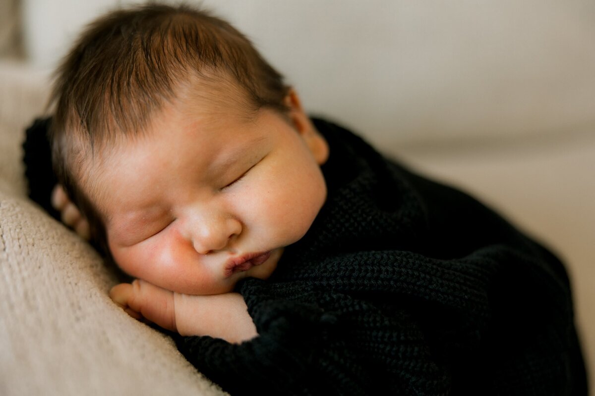 Newborn baby boy in a black sweater laying on the couch.