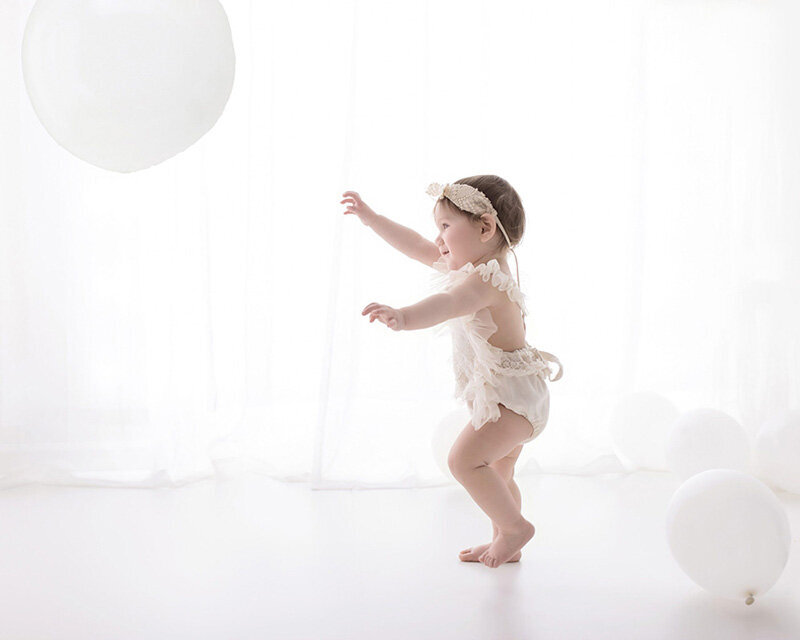A baby girl walking towards a white balloon