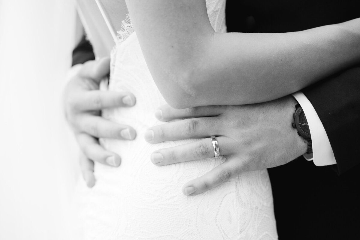 a closeup of a grooms hands on his brides waist
